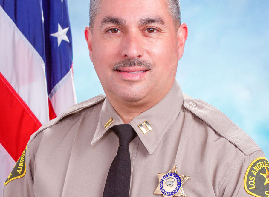Portrait of Captain Mark Reyes in uniform, sitting infront of the American Flag