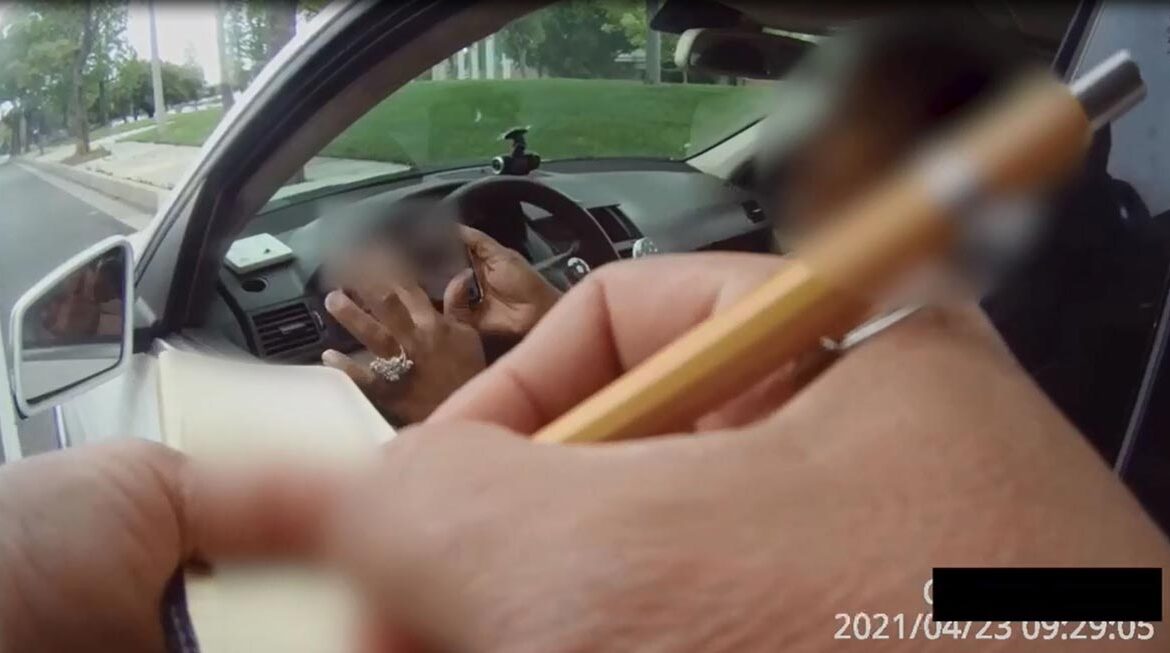 Still image from Body Camera Footage of Deputy writing ticket to a woman inside a car. The Woman is holding up her phone showing the Deputy something on the screen. The image details have been blured to protect the woman's personal information and Identity.