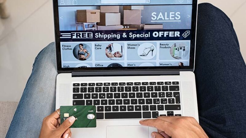 a couple is shopping online, they are sitting on a couch both using a computer. the camera is looking at the computer and keyboard, the wife is holding the credit card and the husband is navigating on the keyboard.