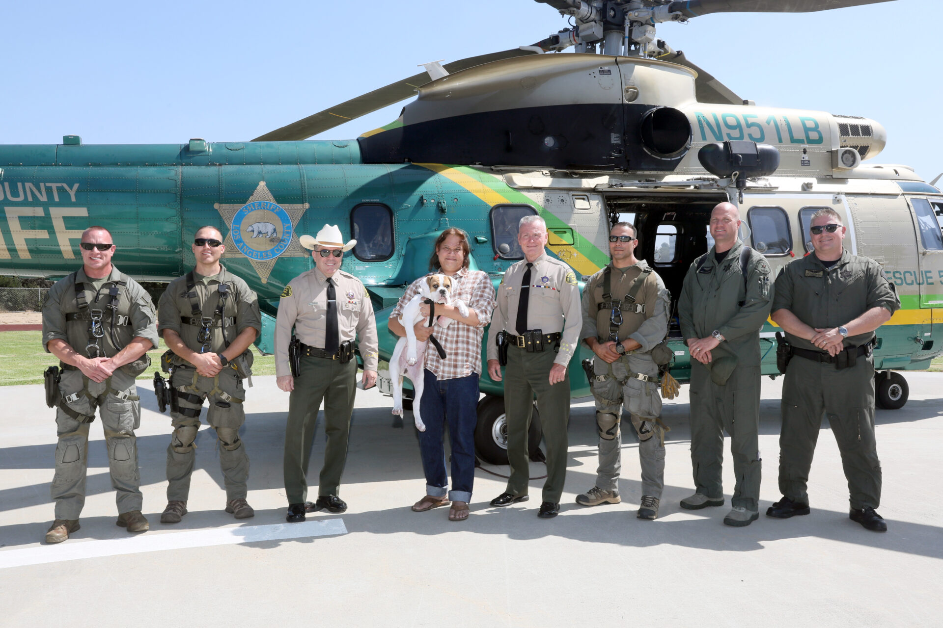 Air 5 Heliocoptor crew stands with Sheriff Villanueva and the rescued hiker and his dog infornt of the large green and gold heliocoptor.