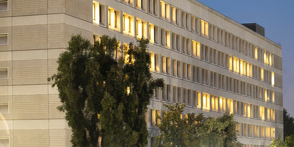 Bechtel building in Norwalk. Beige block building with narrow lit windows lined by trees.