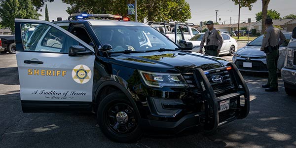 Black and white SUV with passenger door open in a parking lot. Two deputies are walking around the vehicle inspecting another car.